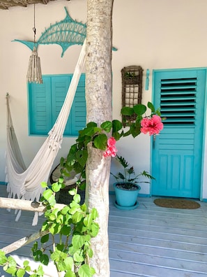 Relax in a serene outdoor space with a hammock and potted plant, surrounded by a tranquil atmosphere and a distinctive blue door.