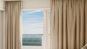 Une chambre à coucher avec un lit, des rideaux et une vue sur un immeuble par la fenêtre.