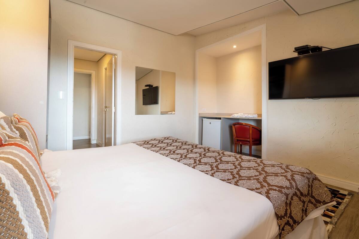 Une chambre d’hôtel équipée d’un lit, d’un bureau, d’une chaise, d’une télévision et d’un miroir.