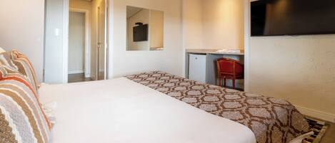 Habitación de hotel con cama, escritorio, silla, televisor y espejo.