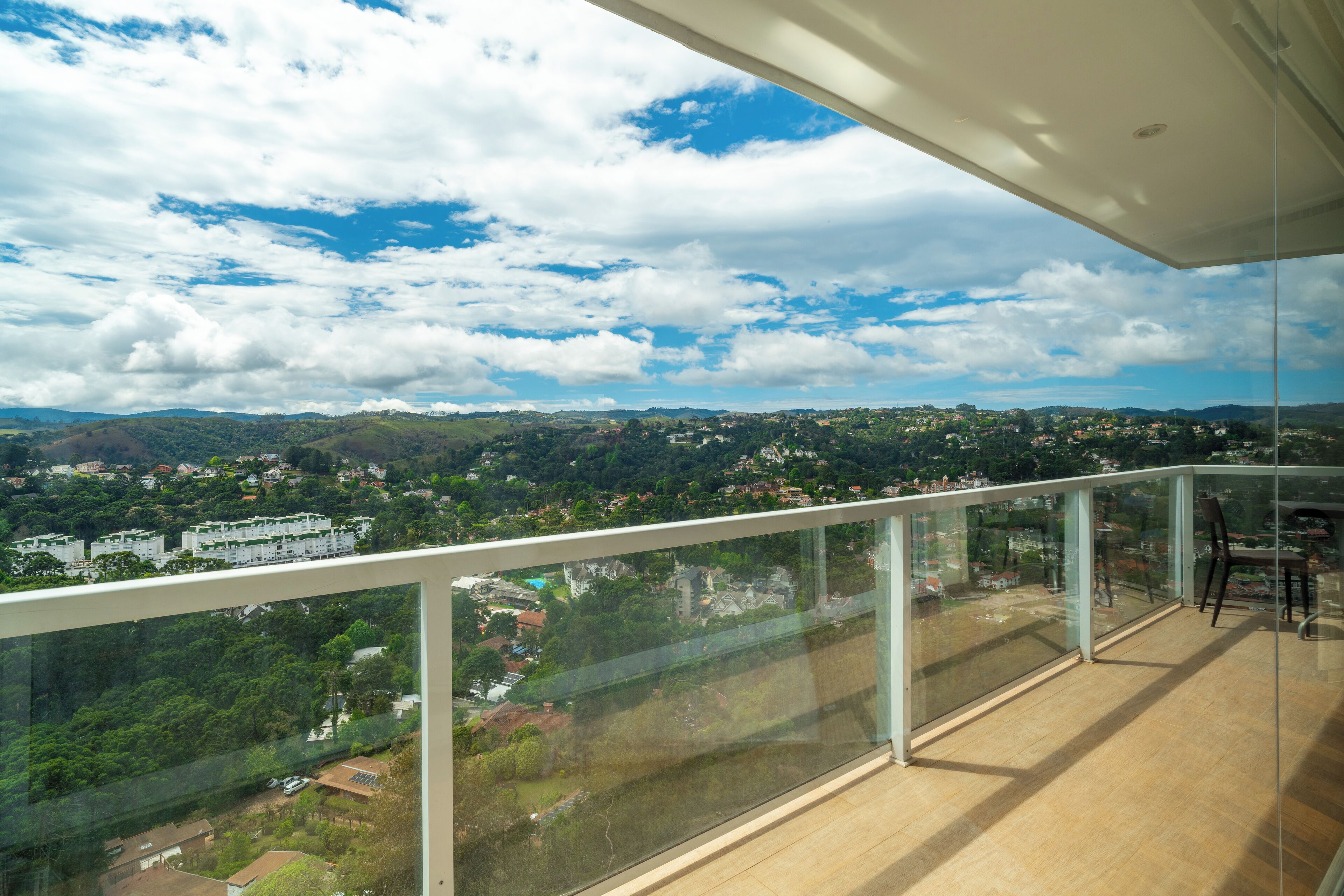 A balcony with a glass railing overlooking a cityscape with buildings and greenery.