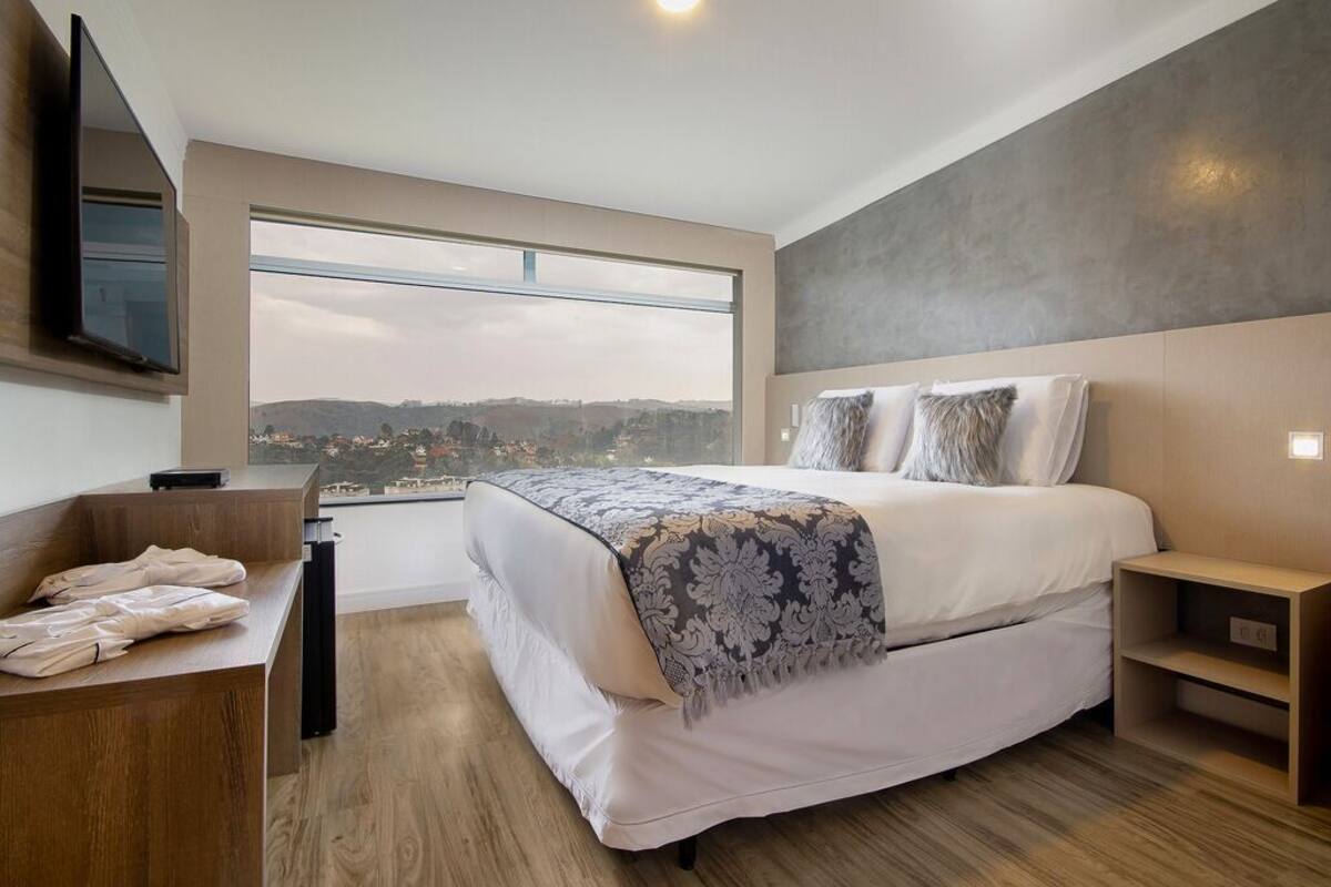 Une chambre d’hôtel moderne, dotée d’un grand lit, d’un bureau et offrant une vue sur le paysage urbain.