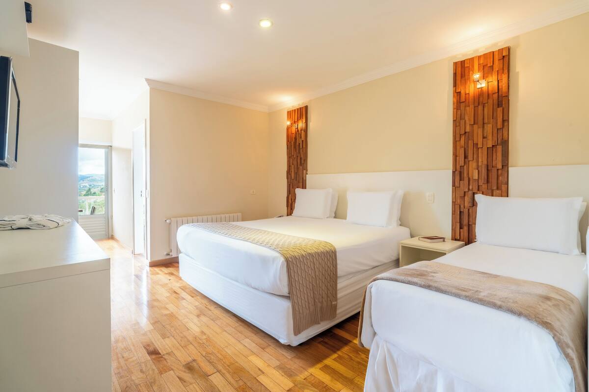 Une chambre d’hôtel avec un grand lit, des tables de chevet, un mur décoratif en bois et une vue sur l’extérieur par une porte ouverte.
