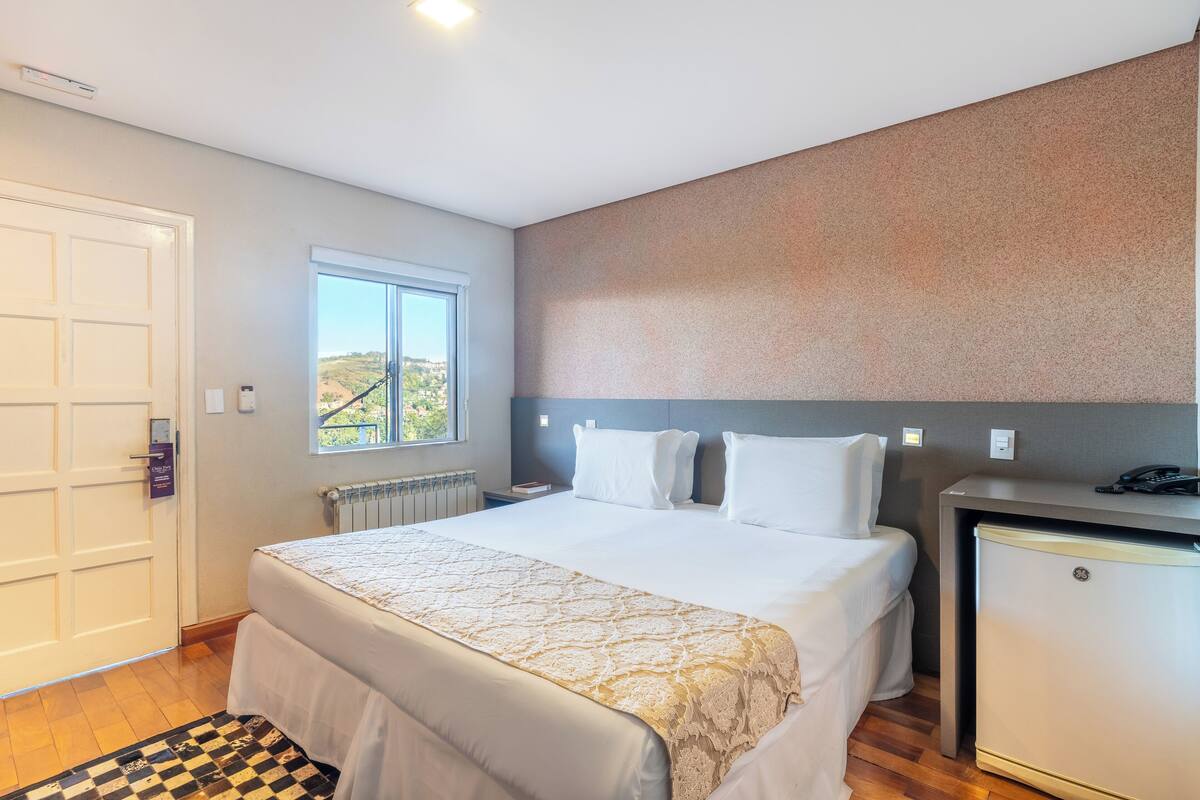 Une chambre d’hôtel avec un lit, un bureau, un réfrigérateur, une fenêtre et une porte.