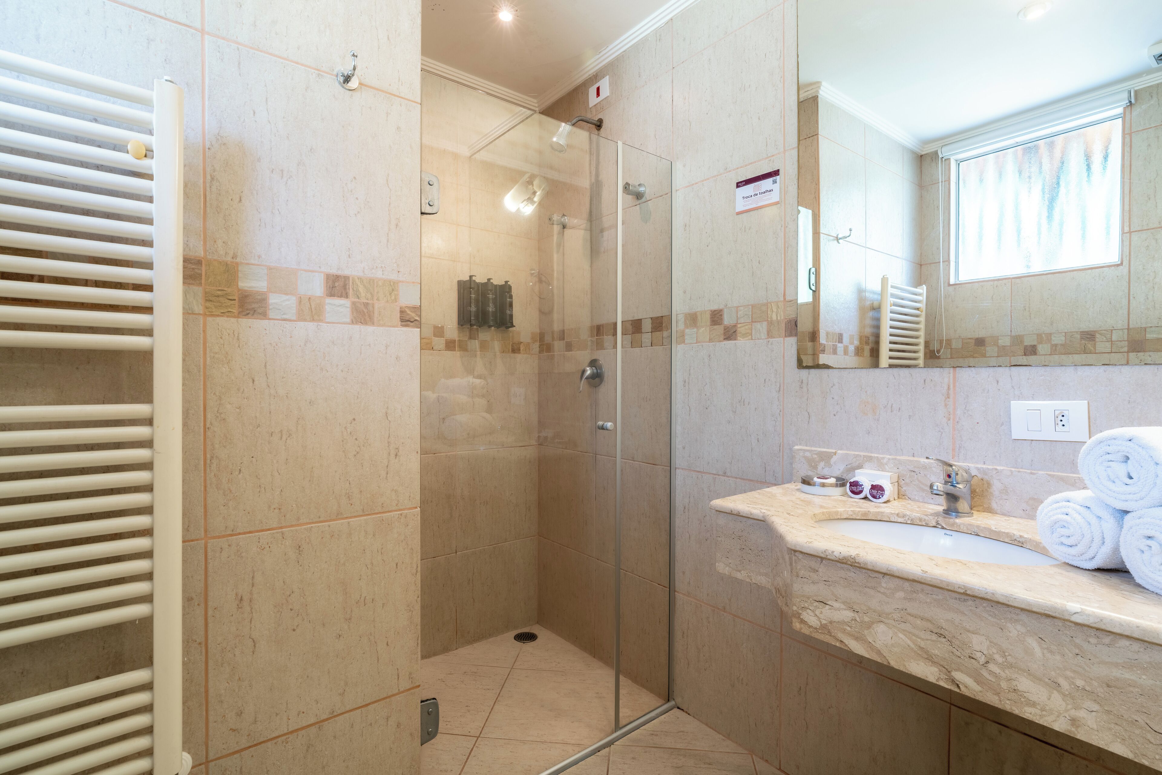 A bathroom with a glass-enclosed shower, a marble sink, and a towel rack.