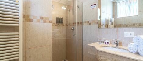 A bathroom with a glass-enclosed shower, a marble sink, and a towel rack.