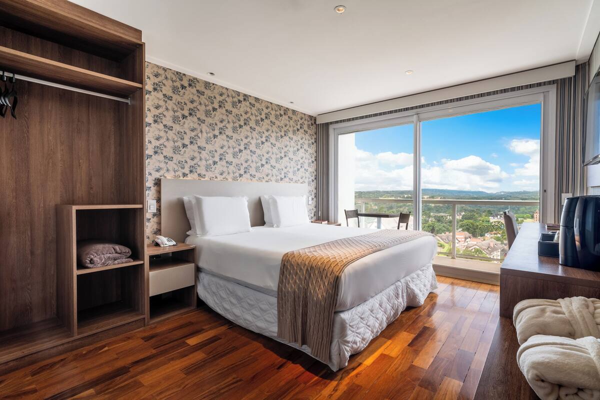 Une chambre dotée d’un grand lit, d’un plancher en bois, d’une armoire, d’un bureau et offrant une vue sur le paysage grâce à de grandes fenêtres.