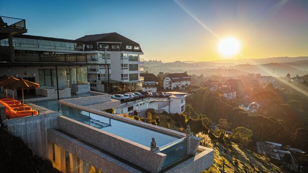 Un hôtel moderne doté d’une piscine à débordement sur le toit, d’une façade en verre et offrant une vue sur le paysage environnant au coucher du soleil.