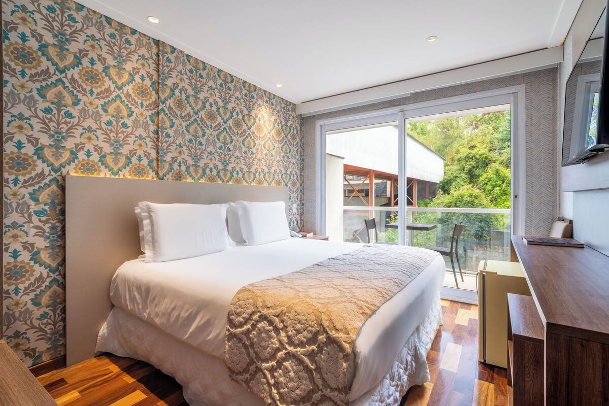 Une chambre avec un grand lit, un bureau et une vue sur la verdure.