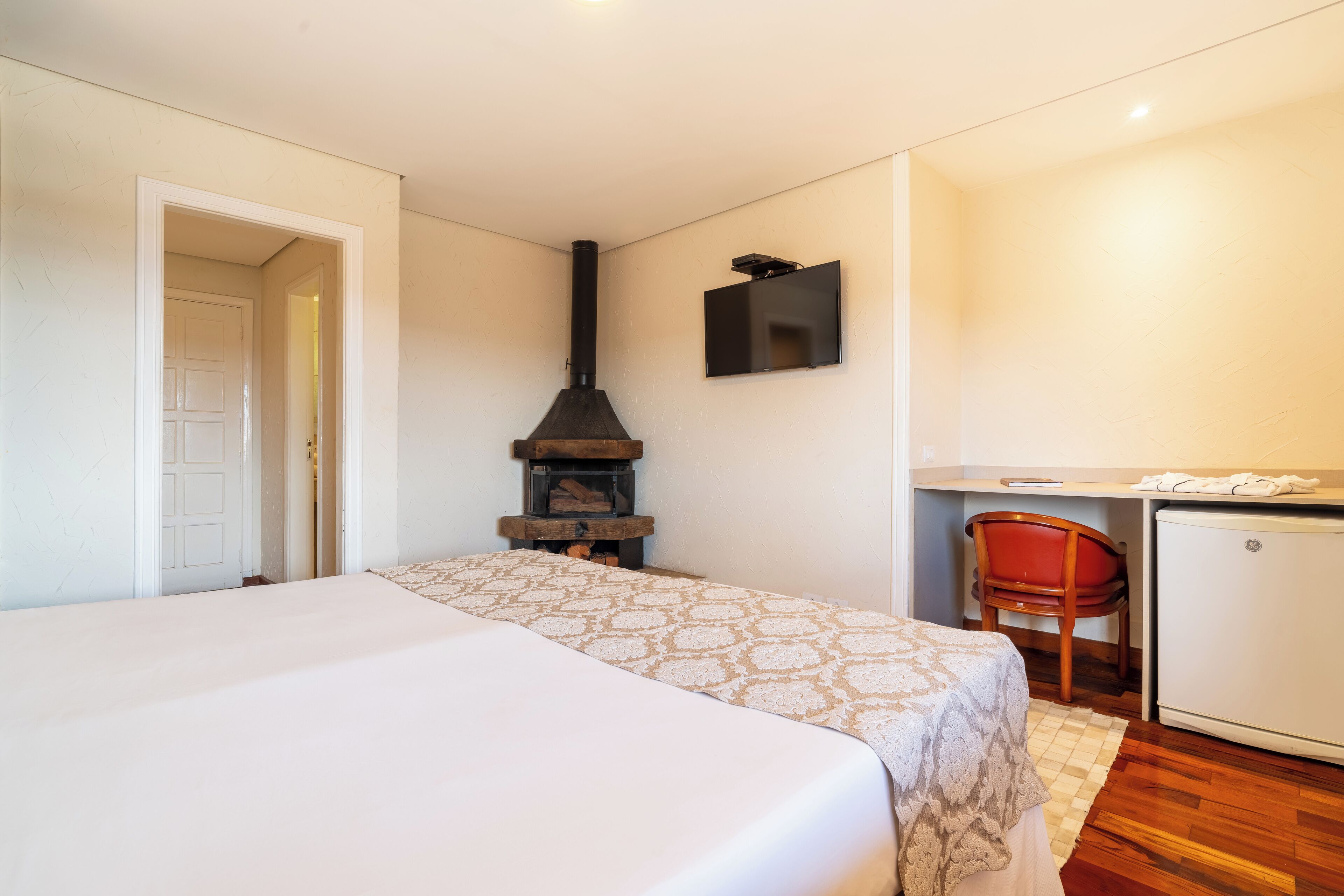 A bedroom with a bed, a fireplace, a desk, and a chair.