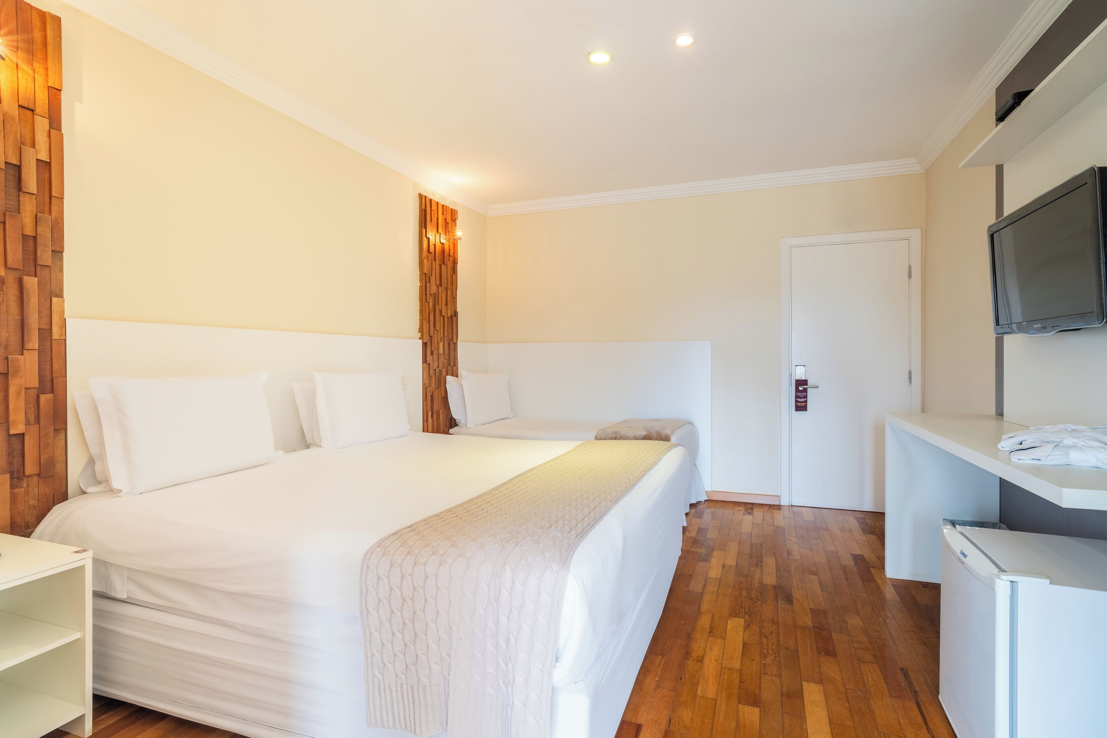 A hotel room with a large bed, a desk, a TV, and a door.