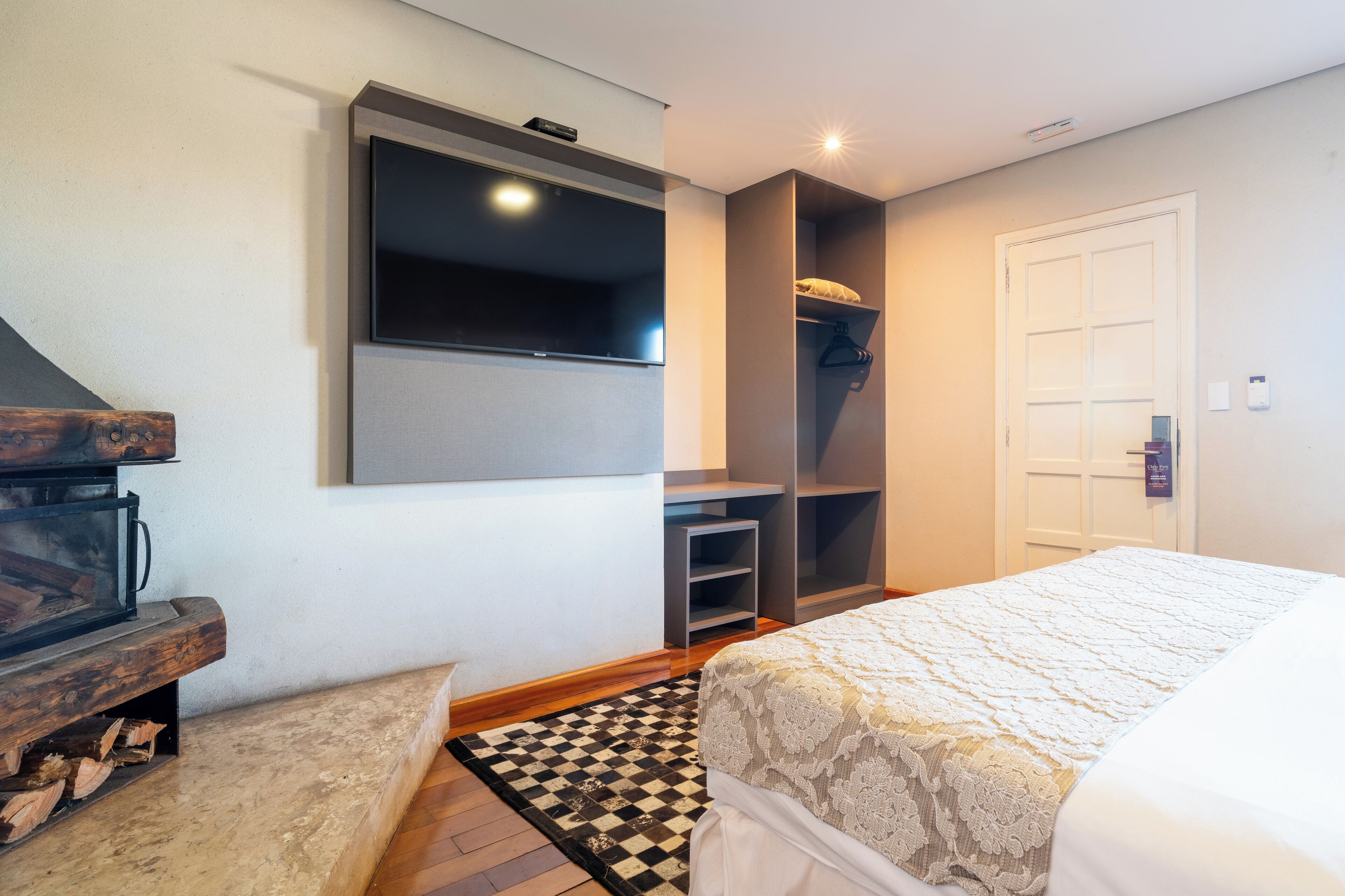 A bedroom with a bed, a TV mounted on the wall, a wooden bench, and a checkered rug.