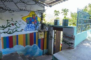 A colorful mural with a house and text, a gated entrance, and a small plant on a ledge. - Pousada Estrelas da Babilonia (Rio de Janeiro)