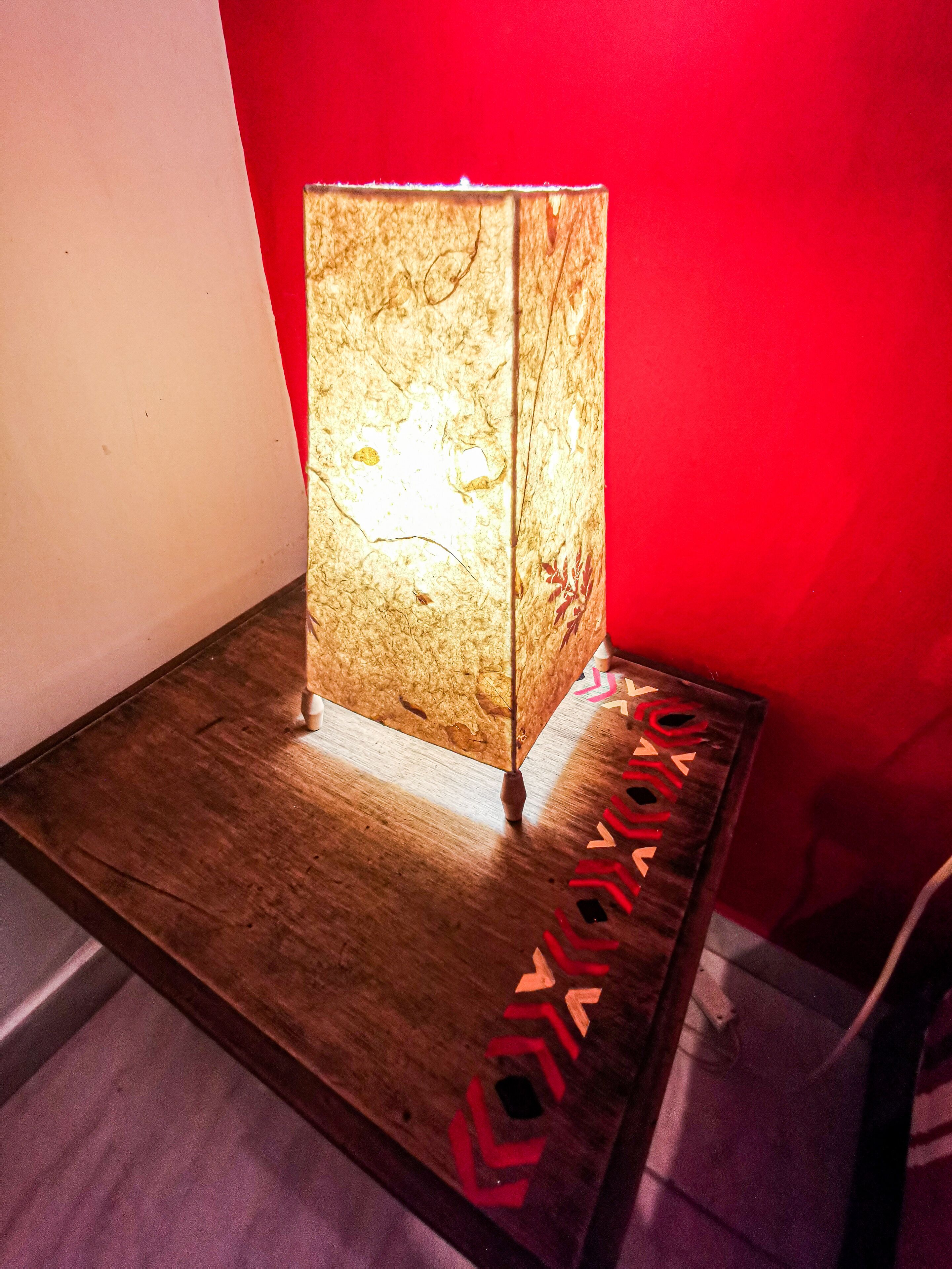 A wooden table with a lamp on it, placed against a red wall.