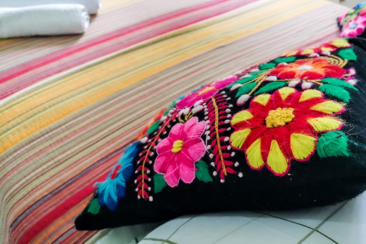 Un coussin orné de broderies florales colorées, posé sur un couvre-lit à rayures.