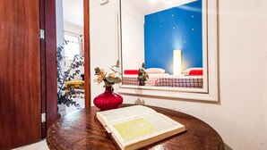 A wooden table with a book and a red vase. A mirror reflects a room with a bed and a night sky view. - Pousada Estrelas da Babilonia (Rio de Janeiro)