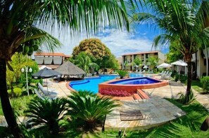 A resort pool area with a hot tub, lounge chairs, and umbrellas.