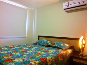 A bedroom with a floral bedspread, a bedside lamp, and an air conditioning unit on the wall. - Solar De Pipa Duplex Flat (Tibau do Sul)