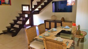 A dining area with a glass table, wicker chairs, and a staircase. - Solar De Pipa Duplex Flat (Tibau do Sul)