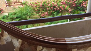 A hammock on a balcony with a view of a brick wall and flowering plants. - Solar De Pipa Duplex Flat (Tibau do Sul)