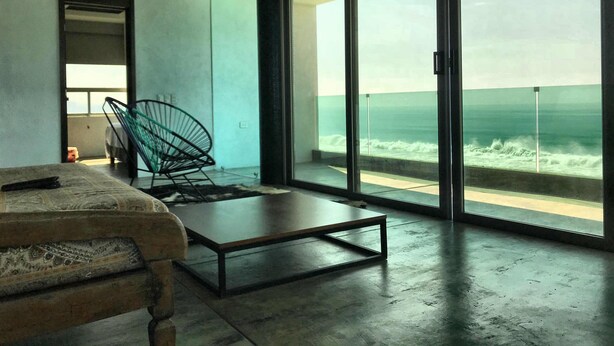 A modern room with a large glass door leading to a balcony with a view of the ocean.