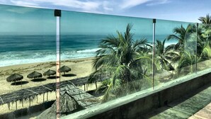 A beach view with palm trees and thatched umbrellas.