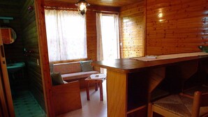 A wooden cabin interior with a wooden bench, a small table, and a bar area.