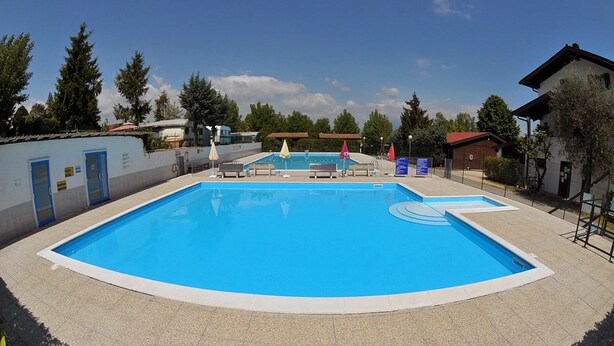 A rectangular swimming pool with a blue interior, surrounded by a tiled deck. There are lounge chairs and umbrellas around the pool.