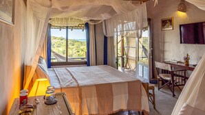 A bedroom with a bed, a desk, and a chair. There is a window with a view of greenery. - Pousada Mar à Vista (Porto Seguro)