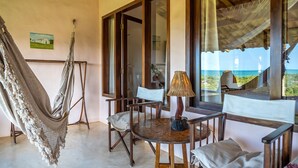 A cozy room with a hammock, a round wooden table with chairs, and a view of the ocean through large windows. - Pousada Mar à Vista (Porto Seguro)