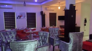 Uma sala de estar com poltronas confortáveis, um espaço de jantar com mesa posta para dois e uma televisão fixada na parede.