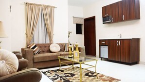 A living room with a sofa, coffee table, and a rug. There is a kitchen area with cabinets and a microwave. - Rightgate Hotel & Suites (Lagos)
