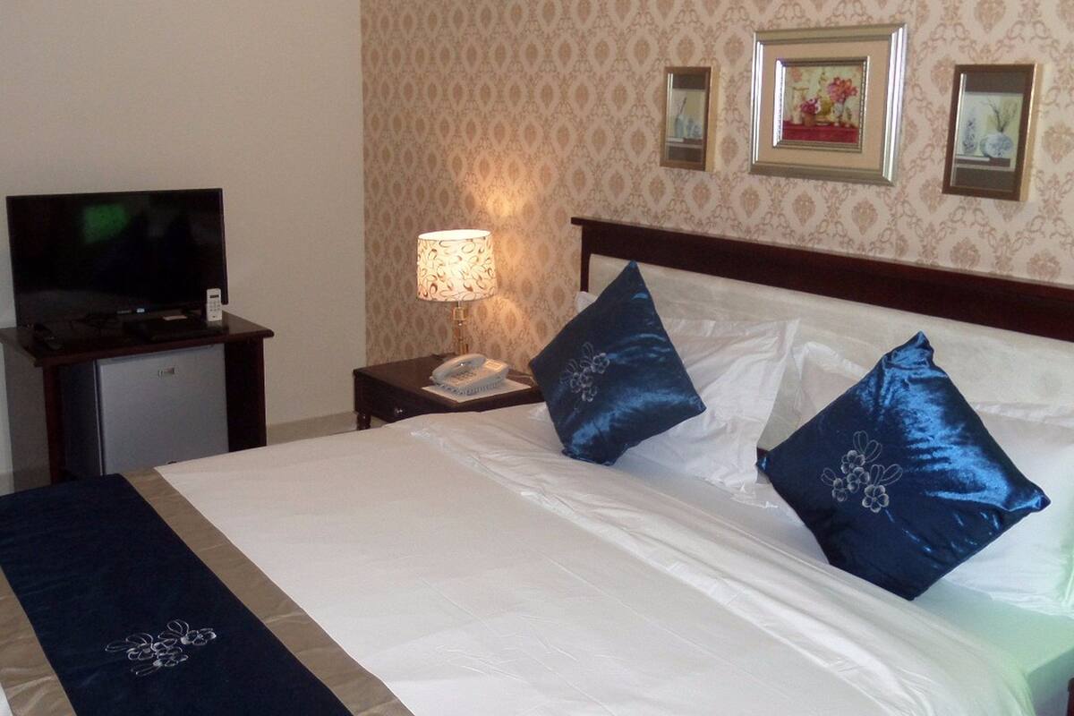 A hotel room with a bed, a TV, a lamp, and framed pictures on the wall.