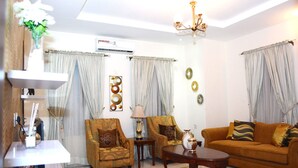 A living room with a sofa, two armchairs, a coffee table, a lamp, and a vase with flowers. - Rightgate Hotel & Suites (Lagos)