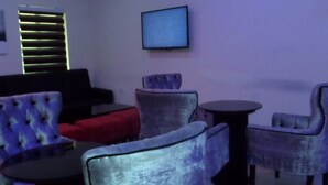 Uma área de estar moderna com assentos confortáveis, uma televisão de tela plana e iluminação ambiente.