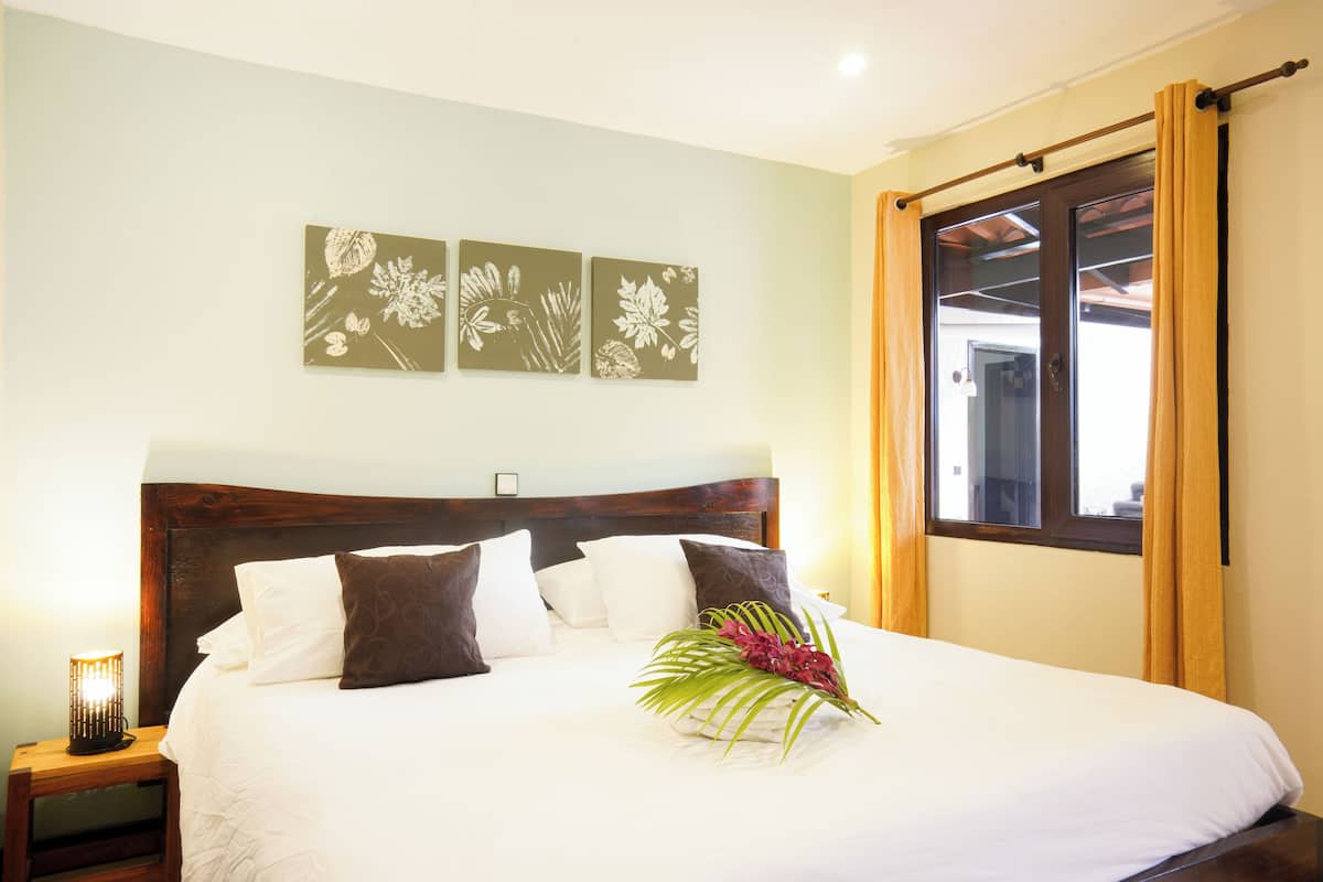 A neatly made bed with white and brown bedding, a decorative wall art piece above it, and a window with curtains.