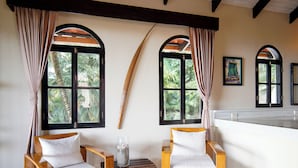 A room with two wooden chairs, a small table with a glass vase, and large windows with curtains. - Casa Marbella (Cóbano)
