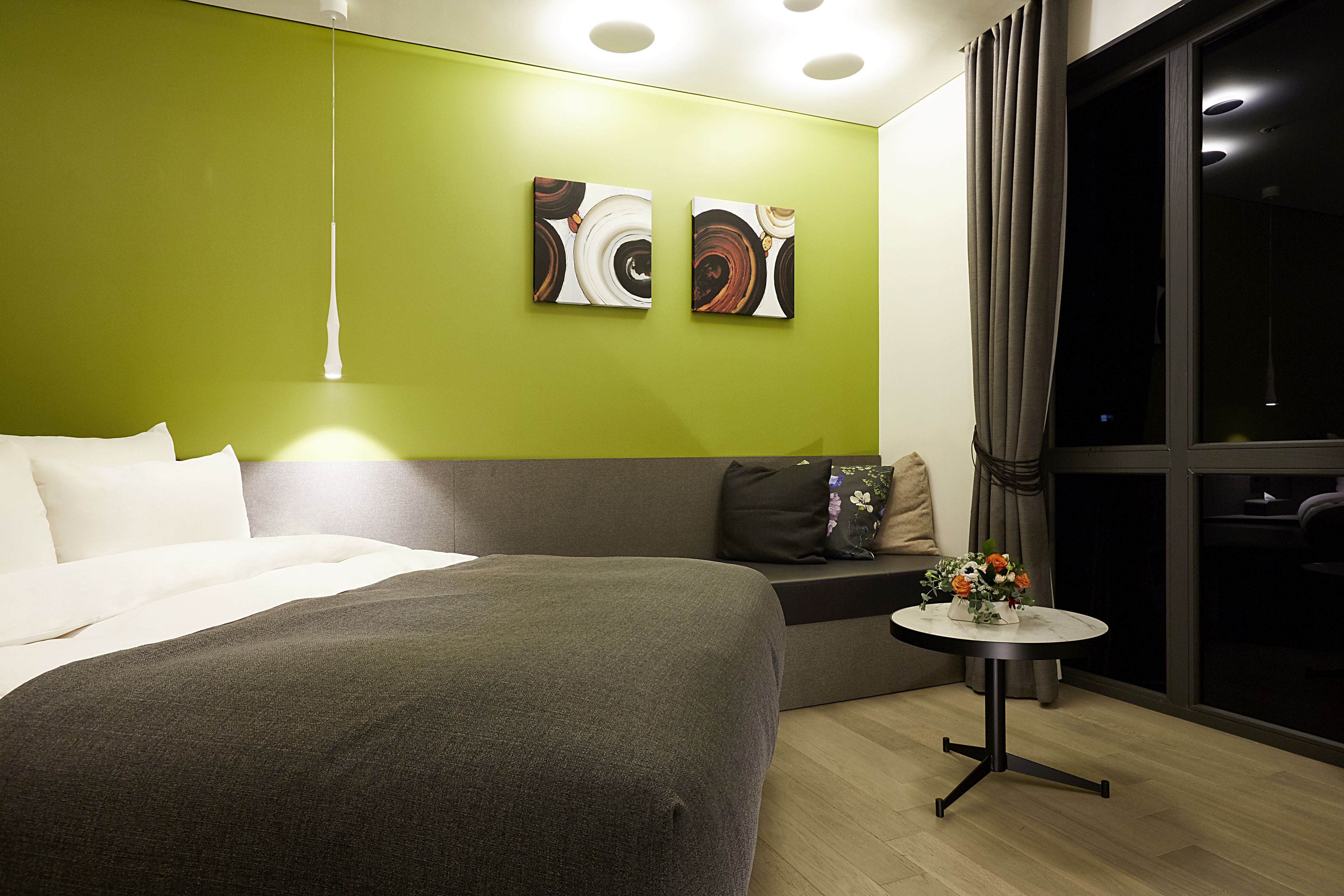 A hotel room with a large bed, a sofa, a small table with flowers, and abstract art on the wall.