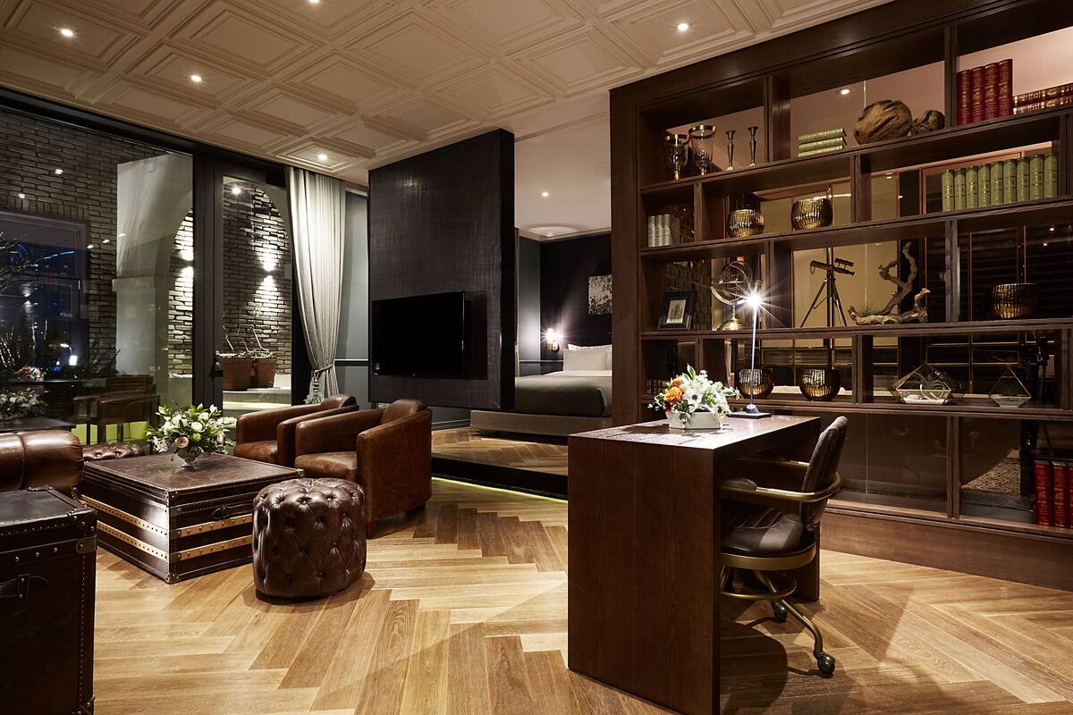 A modern living room with leather furniture, a flat-screen TV, and a bookshelf filled with decorative items.