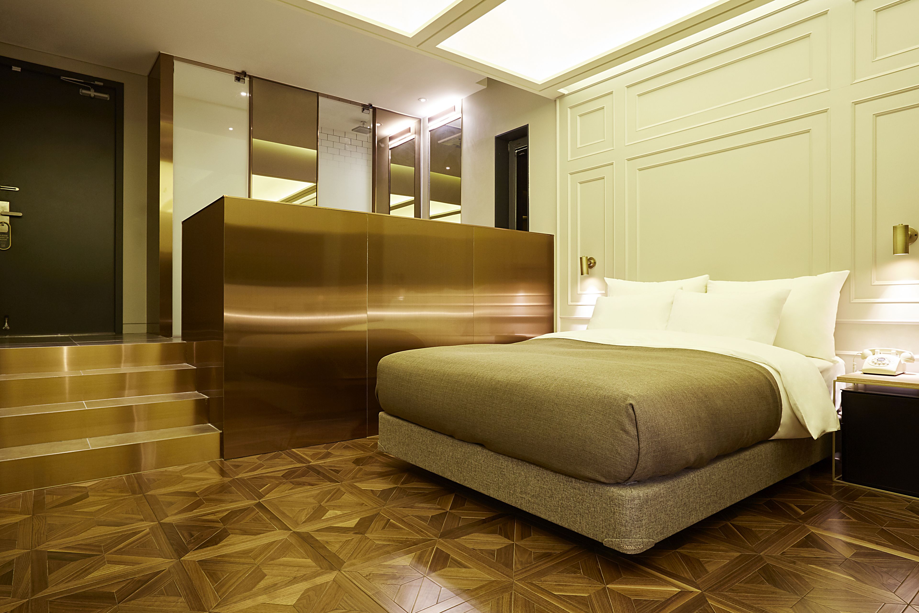 A hotel room with a bed, a nightstand, a mirror, and a staircase leading to a door.