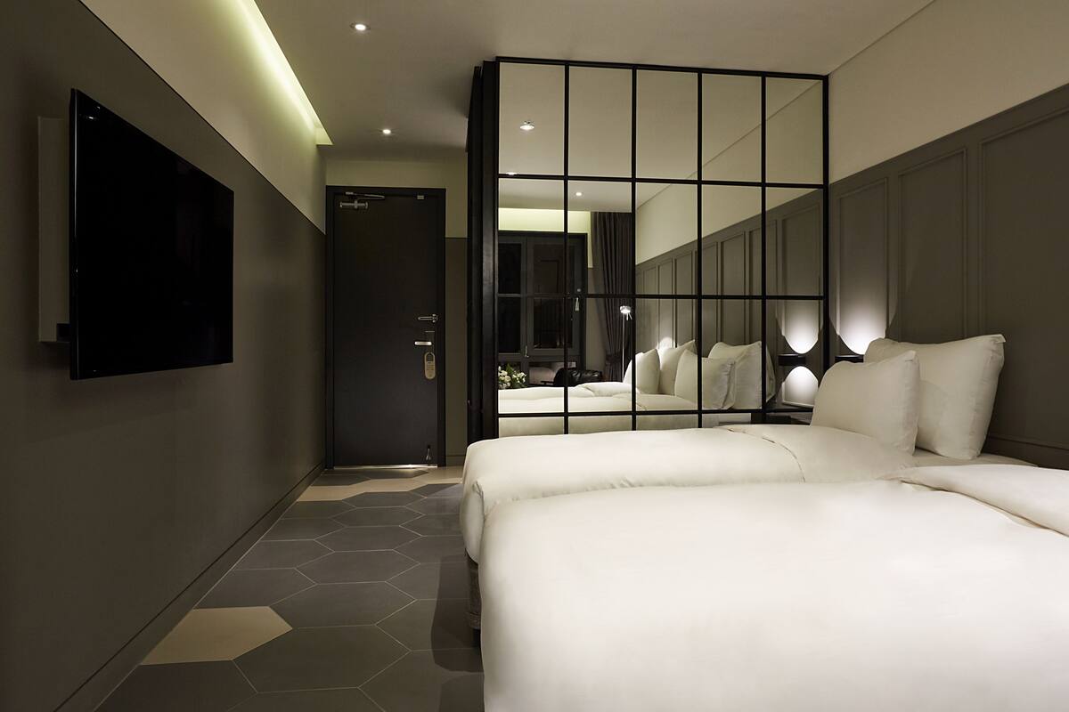 A modern hotel room with a large bed, a TV mounted on the wall, and a mirror reflecting the room.