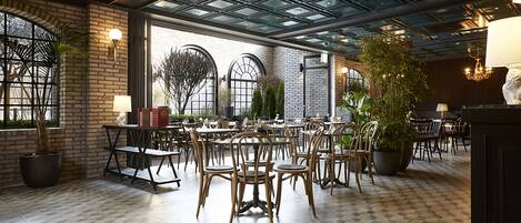 A spacious indoor dining area with brick walls, large windows, and a high ceiling with a glass panel design.