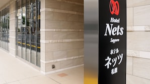 L’entrée d’un hôtel, avec une enseigne indiquant « Hôtel Nets Sapporo » et un logo au-dessus.