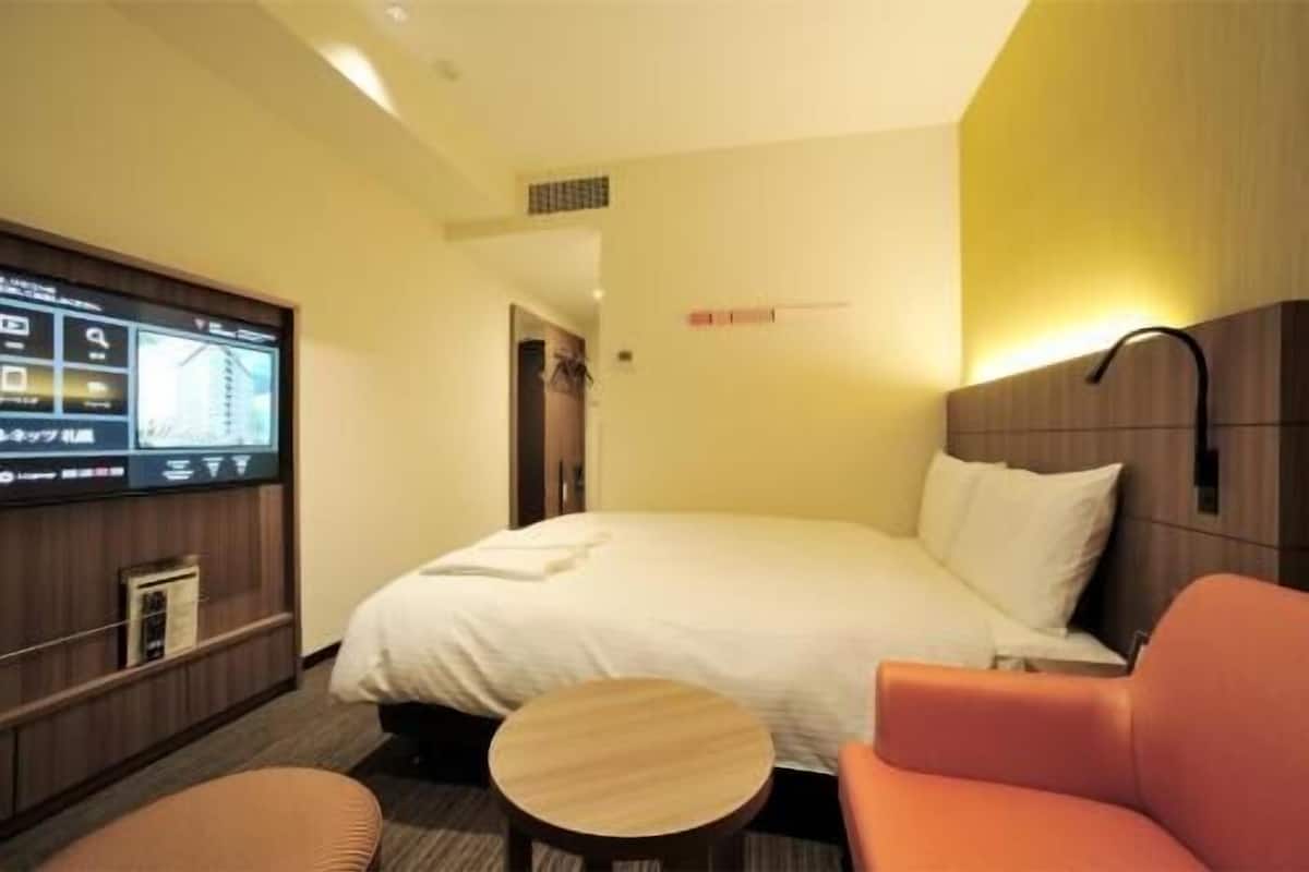 A hotel room with a bed, a TV mounted on the wall, a small round table, and a sofa.