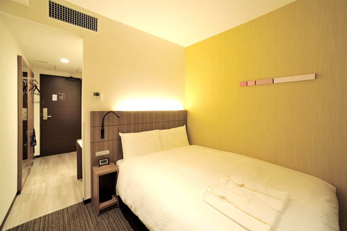 A hotel room with a large bed, a bedside table, a nightstand, a mirror, and a door.