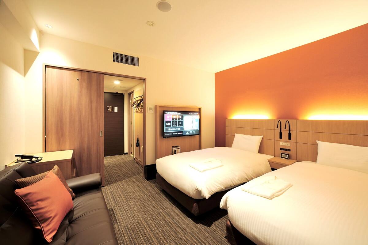 A hotel room with two beds, a sofa, a TV, and a wooden wardrobe.