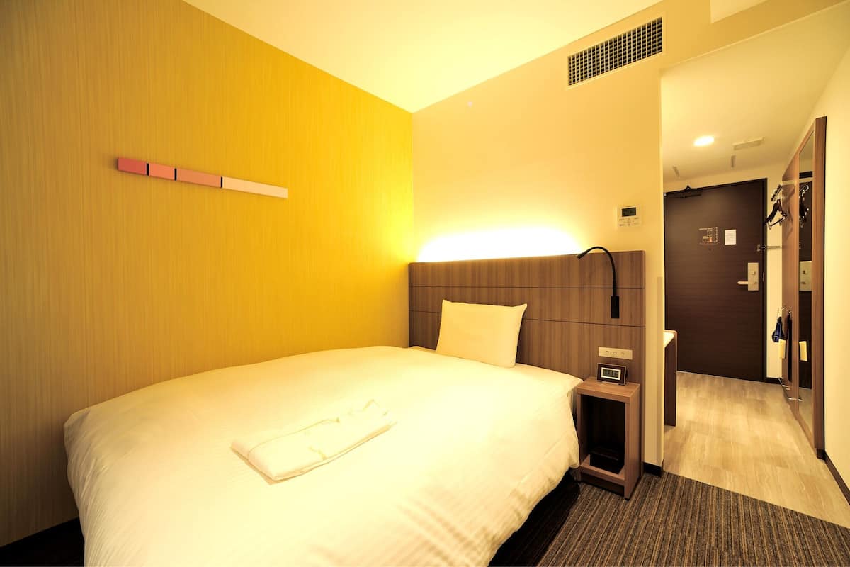 A hotel room with a large bed, a bedside table, a nightstand, a headboard, and a mirror.