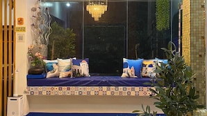 A room with a large window, a blue sofa set, a chandelier, and a tiled wall. - Makiling Onsen Hotel (Los Banos)