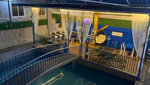 An indoor pool area with a glass barrier, blue railing, and seating arrangements. - Makiling Onsen Hotel (Los Banos)