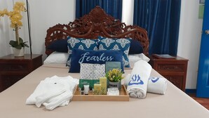 A neatly arranged hotel room with a bed, a bedside table with a plant, and a tray of toiletries including a face mask, soap, and towels. - Makiling Onsen Hotel (Los Banos)